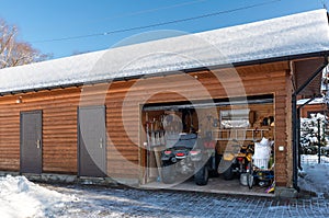 Facade view open door ATV home garage with quad bikes offroad vehicle parked sunny snowy cold winter day. ATV adventure