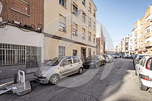 Facades of urban residential housing of modest construction in a street with cars parked in a row