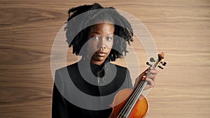 Face, art and violin with black woman musician in studio on wooden wall background for orchestra performance. Portrait