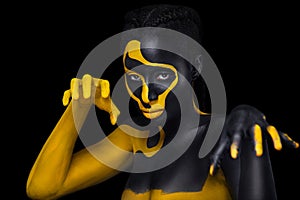 Face art. Woman with black and yellow body paint. Young african girl with colorful bodypaint. An amazing model with