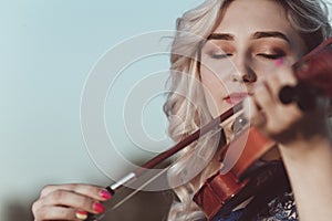 Face of a beautiful girl with a violin under her chin outdoors, romantic young woman playing a musical instrument on nature in