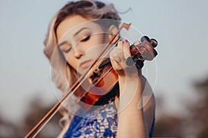 Face of a beautiful girl with a violin under her chin outdoors, romantic young woman playing a musical instrument on nature in