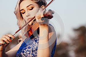 Face of a beautiful girl with a violin under her chin outdoors, romantic young woman playing a musical instrument on nature in