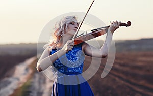 Face of a beautiful girl with a violin under her chin outdoors, young woman playing a musical instrument on nature in solitude,