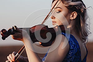 Face of a beautiful girl with a violin under her chin outdoors, young woman playing a musical instrument on nature in solitude,