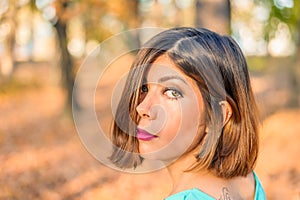 Face of a beautiful young black-haired woman half-covered by hair in a yellow autumn forest