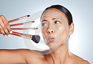 Face, beauty and senior woman with makeup brushes in studio isolated on a gray background. Cosmetics, skincare products