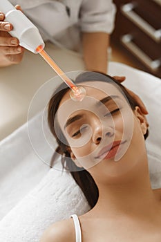 Face Beauty Treatment. Woman Using Darsonval Skin Care Device photo