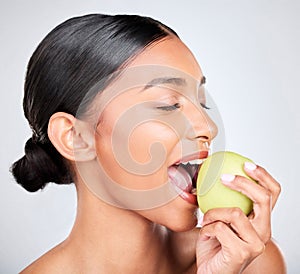 Face, beauty and woman biting an apple for health, wellness or nutrition in studio on white background. Food, skincare