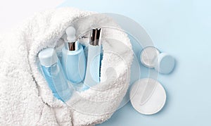 Face care products tonic or lotion, serum, cream, micellar water, cotton pads covered in towel on blue, powder background. photo