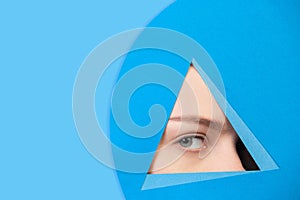 Face of caucasian woman peeking throught triangle in blue background