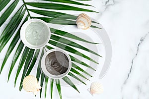 Face clay masks in bowls with tropical palm leaf on marble table. Flat lay, top view. Facial skincare, SPA natural organic