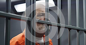 Face close up of elderly prisoner standing behind metal bars in prison cell