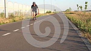 Face close view of man rides longboard sitting at empty straight road. Summer vacation hipster rides skateboard outside