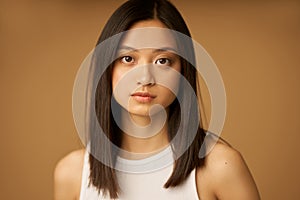 Face closeup of beautiful mixed race young woman with perfect skin looking at camera while standing isolated over brown