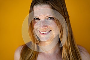 Face closeup of smiling european woman looking to camera. Likeable long-haired lady over yellow background. photo