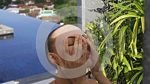 Face closeup of young woman wearing purple sunglasses looking at camera in infinity rooftop swimming pool on a sunny day.