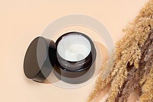 face collagen cream in glass jar and dry flowers reeds on beige background. skin and body care beauty products