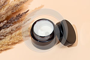 face cream on beige background. Dry ear reeds or pampas grass decoration. Professional bottle for facial and body