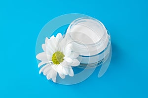 Face cream jar with white chamomile flower on blue background. Herbal lotion in glass bottle, natural cosmetic. Skin care concept