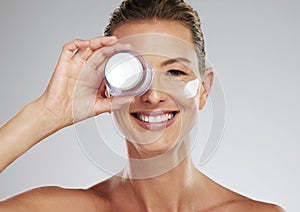 Face cream, skincare and portrait of a mature woman in a studio standing by gray background. Happy, smile and healthy