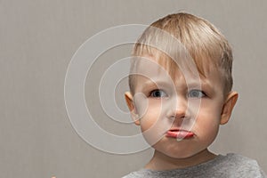 The face of a cute blond boy 3 years old close-up with facial expressions and emotions of an angry and capricious child