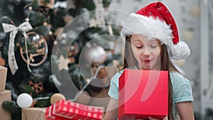 Face of festive wonder cute kid open magic Xmas present with red ribbon posing at decorative spruce