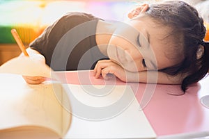 Face focusing of adorable asian child girl is writing on her paper book in the room at home with sunlight shows tired and boring