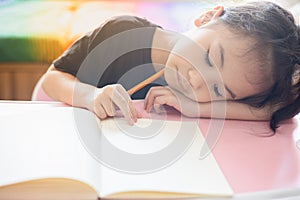 Face focusing of adorable asian child girl is writing on her paper book in the room at home with sunlight shows tired and boring