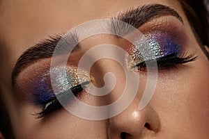 Face of a girl with luxury makeup and perfect skin. She has closed her eyes. Blue and golden eyeshadow, false eyelashes