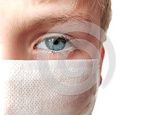 Face of a handsome white seven year old boy in a white protective surgical mask. Eye with a light gray iris. Half face. Blonde