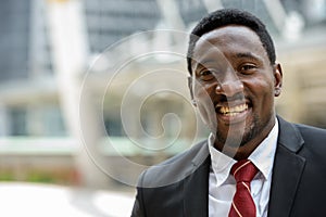 Face of happy young handsome African businessman smiling in the city