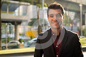 Face of happy young handsome Hispanic businessman smiling in the city