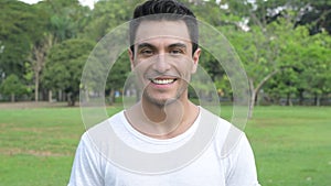 Face of happy young handsome Hispanic man smiling at the park