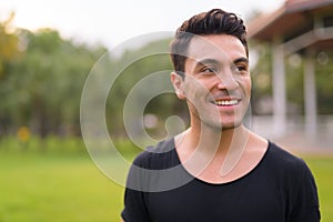 Face of happy young handsome Hispanic man thinking at the park