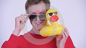 Face of happy young handsome man with sunglasses holding inflatable duck