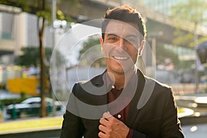 Face of happy young Hispanic businessman smiling in the city outdoors
