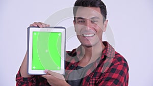 Face of happy young Hispanic hipster man showing digital tablet
