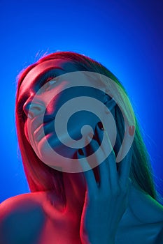 Face lifting. Portrait of beautiful young woman in her 20s with blonde hair, smooth skin and bare shoulders against blue