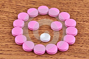 Face made of pink and white pills on wooden background