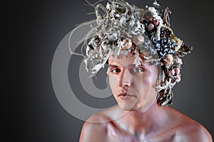 The face of a male model in a headdress of flowers filled with wax