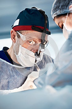 The face of a male surgeon during the operation, close-up head light, a doctor in a mask, glasses makes a life-saving
