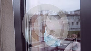 Face of a man in a medical mask in the window, behind glass, street reflection on the glass, camera tracking