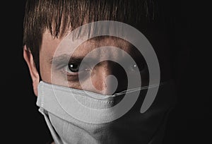 Face of a man in a medical protective mask close-up on a black background. Coronavirus epidemic.