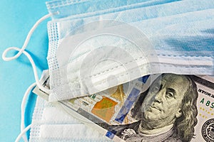 Face mask and banknote of 100 dollars on blue background. Concept of deficit, speculation and shortage of medical masks