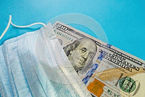 Face mask and banknote of 100 dollars on blue background. Concept of deficit, speculation and sold out of medical masks