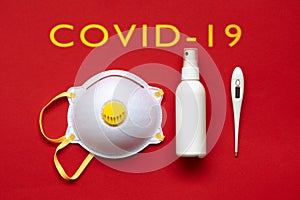 Face mask, bottle with hand sanitizer and thermometer on red background photo