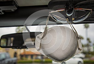 Face mask clipped with sunglasses on visor of interior of a car in a shopping center parking lot during the Coronavirus pandemic