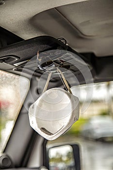 Face mask clipped with sunglasses on visor of interior of a car in a shopping center parking lot during the Coronavirus pandemic