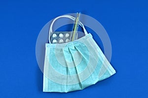 Face mask with medical thermometer and pills on a blue background